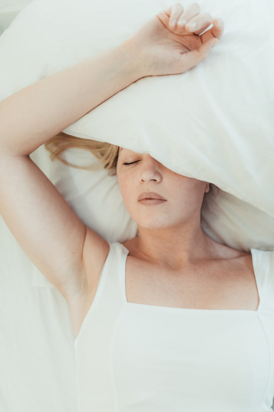 woman-lays-in-a-bed-with-a-pillow-over-her-head